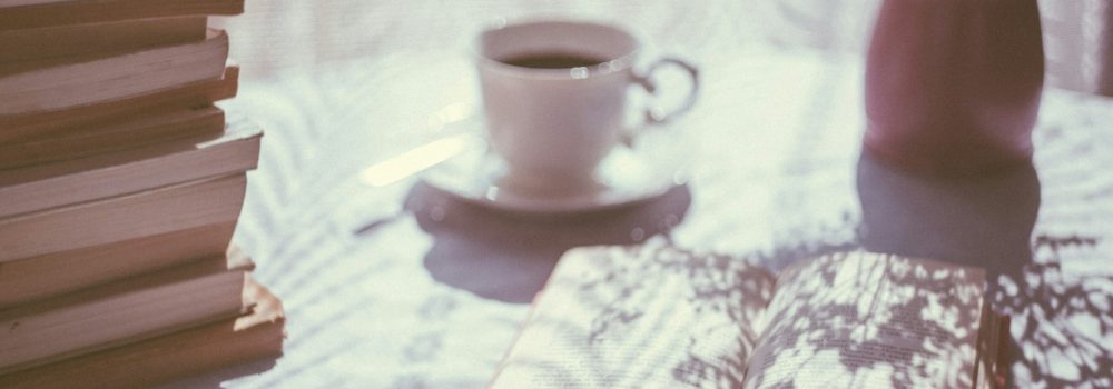 Pial di libri su un tavolo con una tazza di caffè e un libro aperto Foto di freestocks su Unsplash